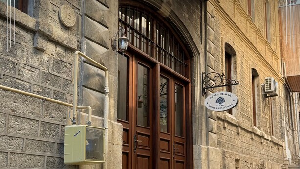 A stone building with a wooden double door, a sign reading "Perla De Mar Hotel & Restaurant," and a small outdoor staircase leading to the entrance. - Gold Perla De Mar Hotel (Baku)