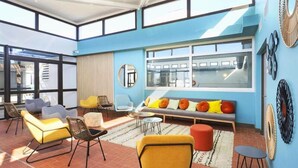 A bright, sunlit room with a blue wall, a sofa with colorful cushions, and a large window. - House in Leucate Near Mediterranean Beach (Leucate)