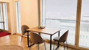 A room with a wooden table and four chairs, large windows with blinds, and a view of a cityscape. - Nordic home bliss with music moments (Helsinki)