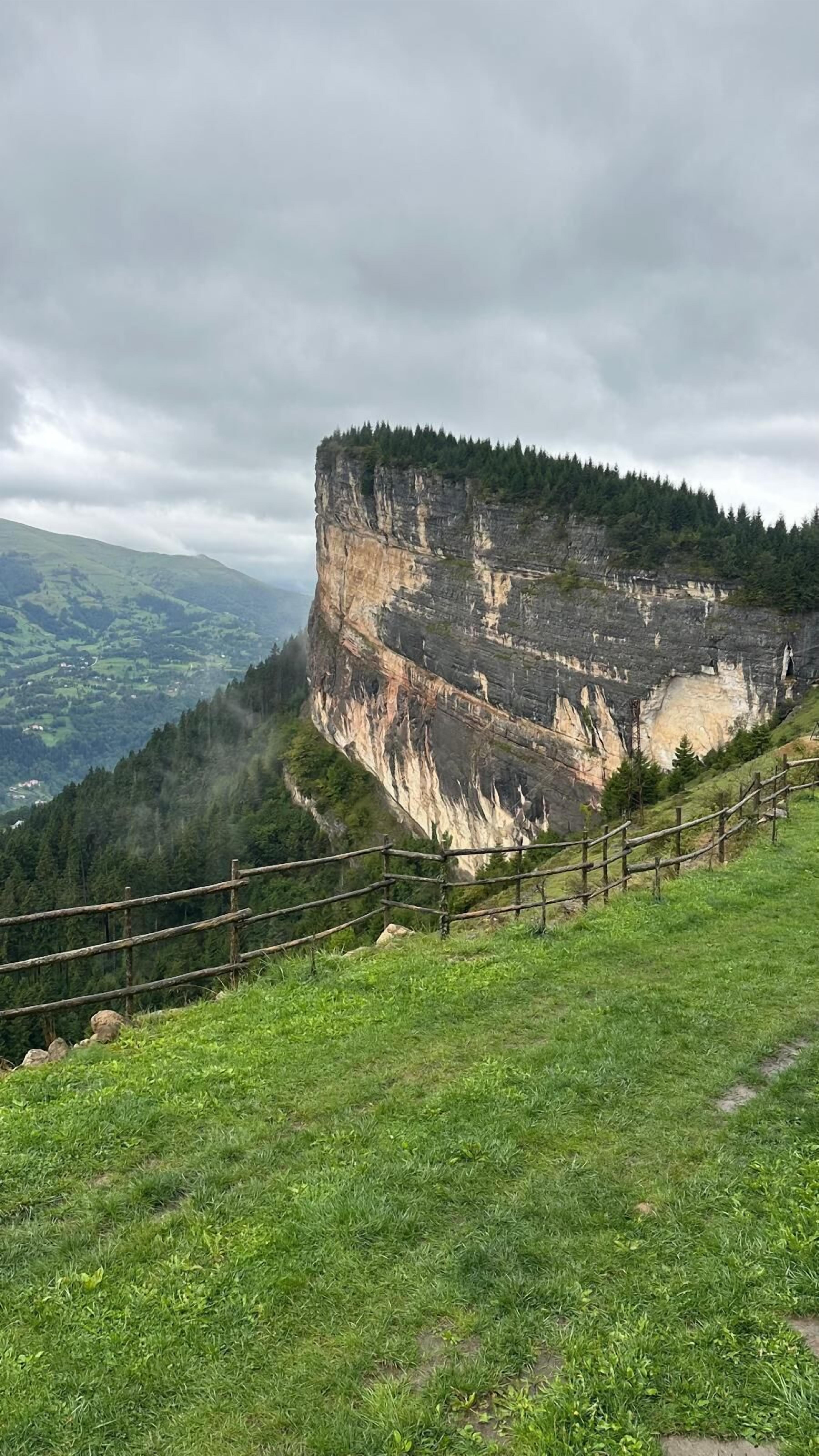 Ein grasbewachsener Hügel mit Holzzaun und einer steilen Klippe.