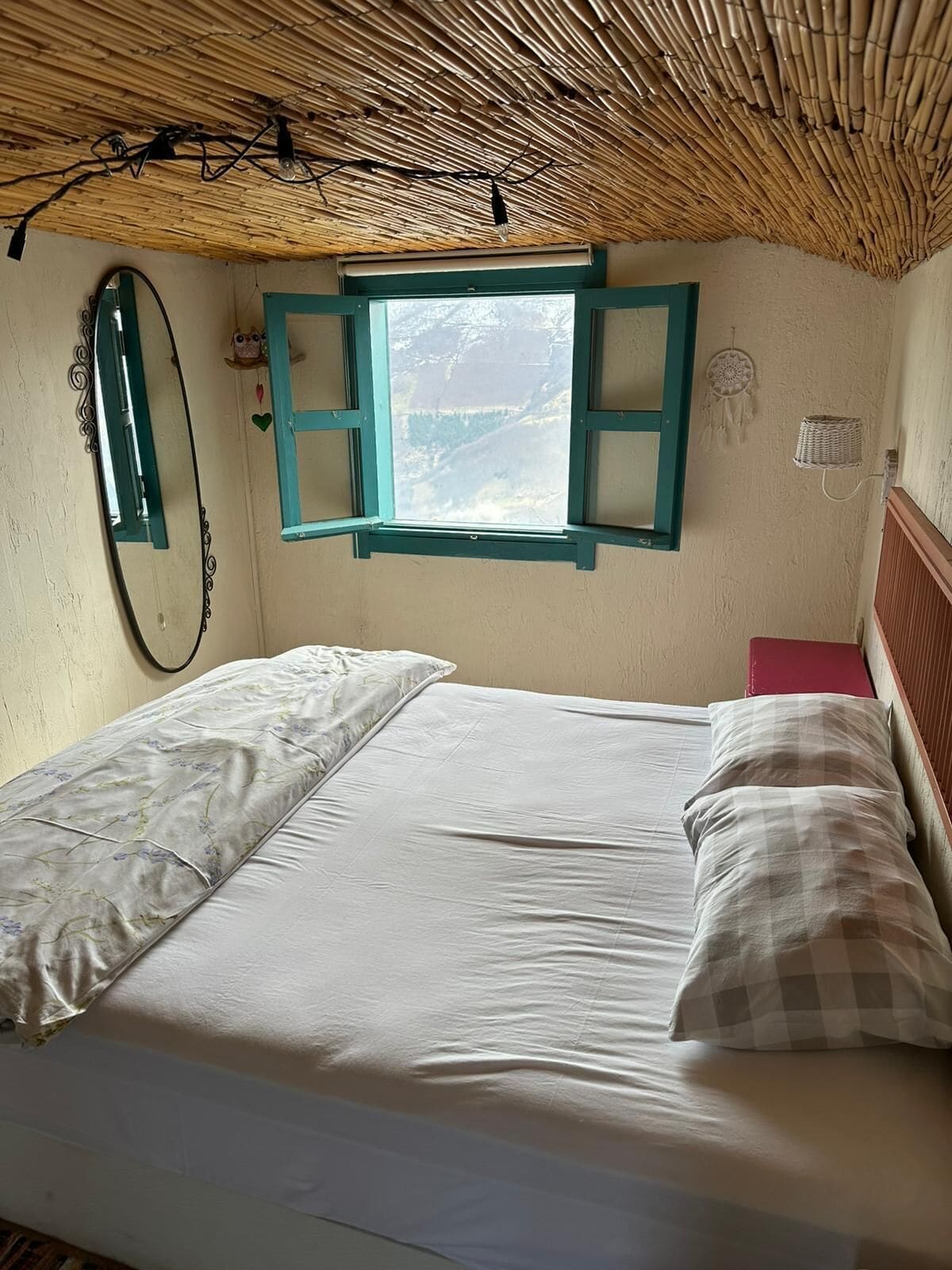 Una cama con ventana, espejo y un atrapasueños en la pared.
