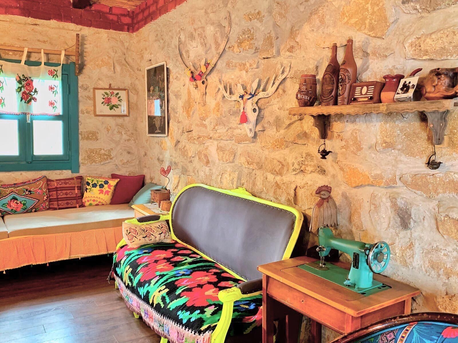 A rustic room with a stone wall, a wooden bench with colorful cushions, a sewing machine, and various decorative items.