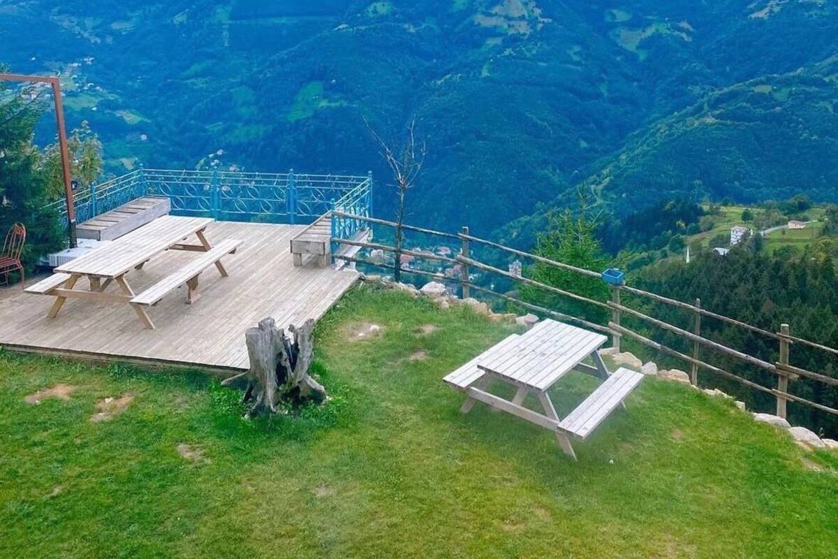 Une terrasse en bois avec des tables de pique-nique, offrant une vue sur un paysage montagneux.