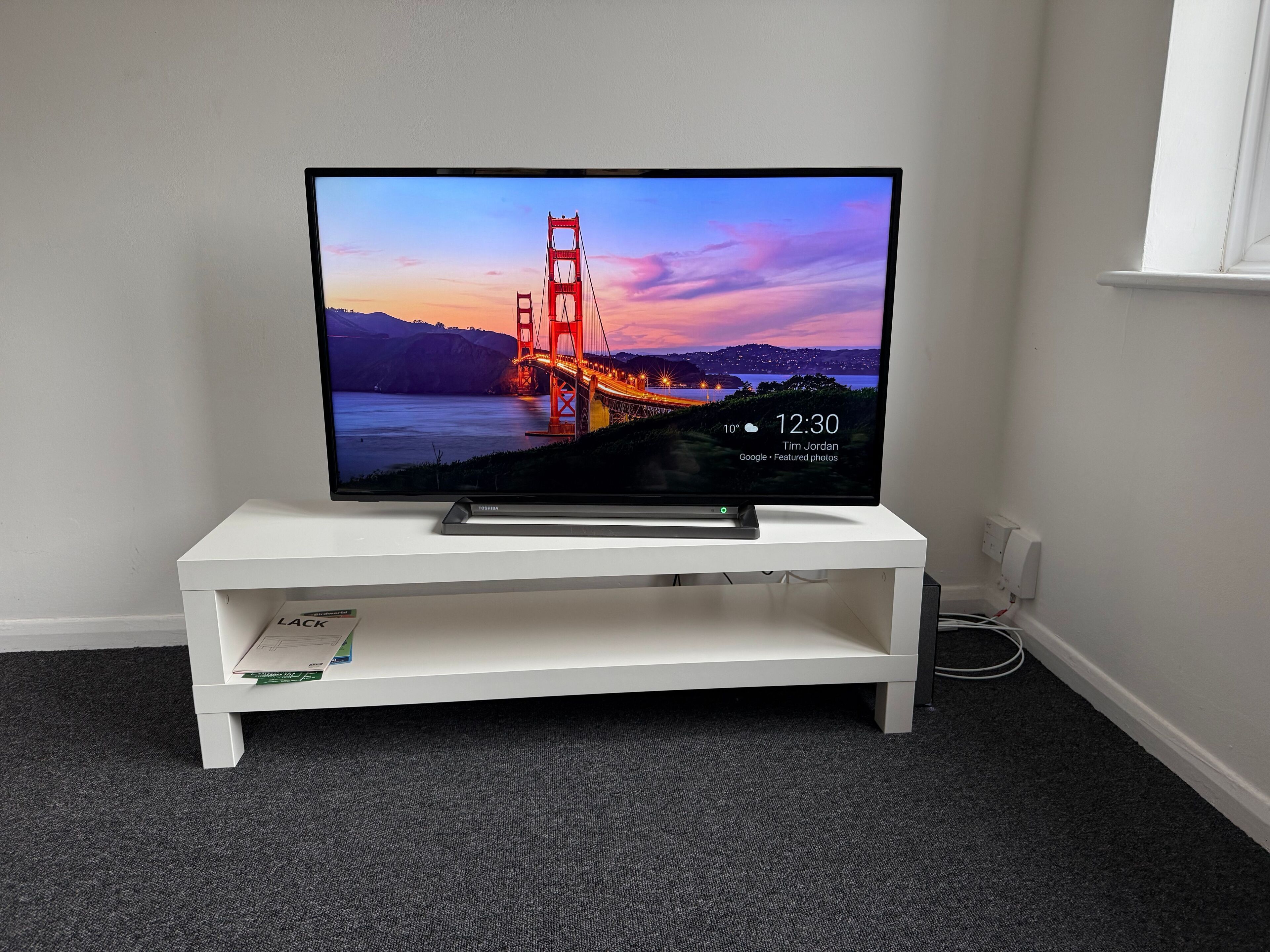 Una TV a schermo piatto su un mobile bianco in una stanza con pavimento in moquette.