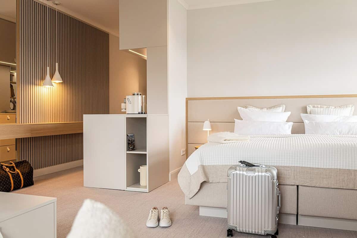 A modern hotel room with a bed, a wardrobe, a desk, and a suitcase.