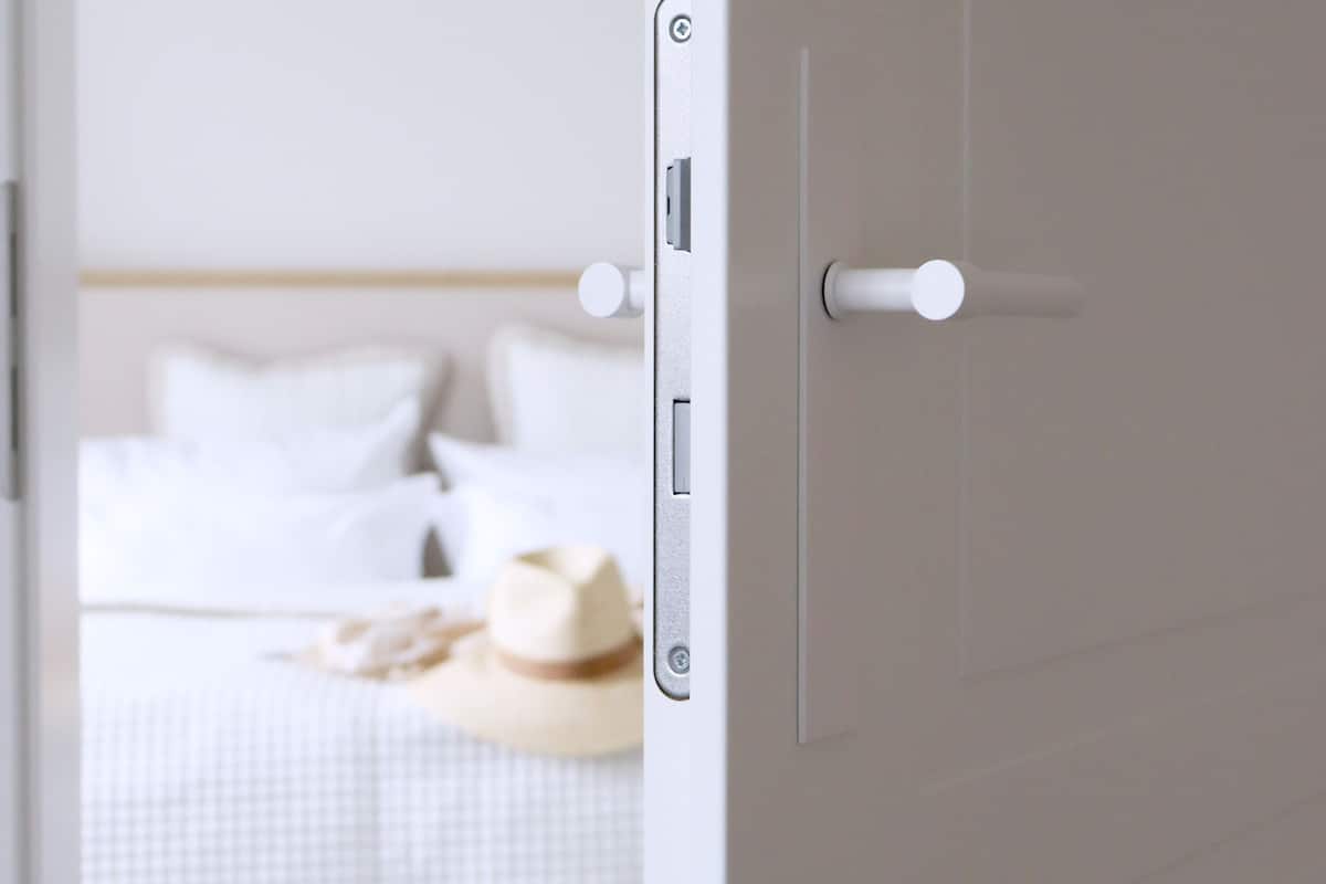 A hotel room with a bed, a nightstand, and a door with a handle.