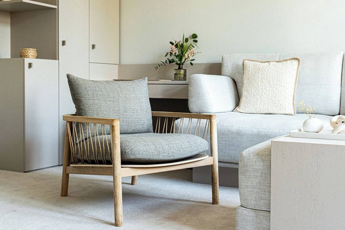 A modern living room with a wooden chair, a grey sofa, and a small table with decorative items.