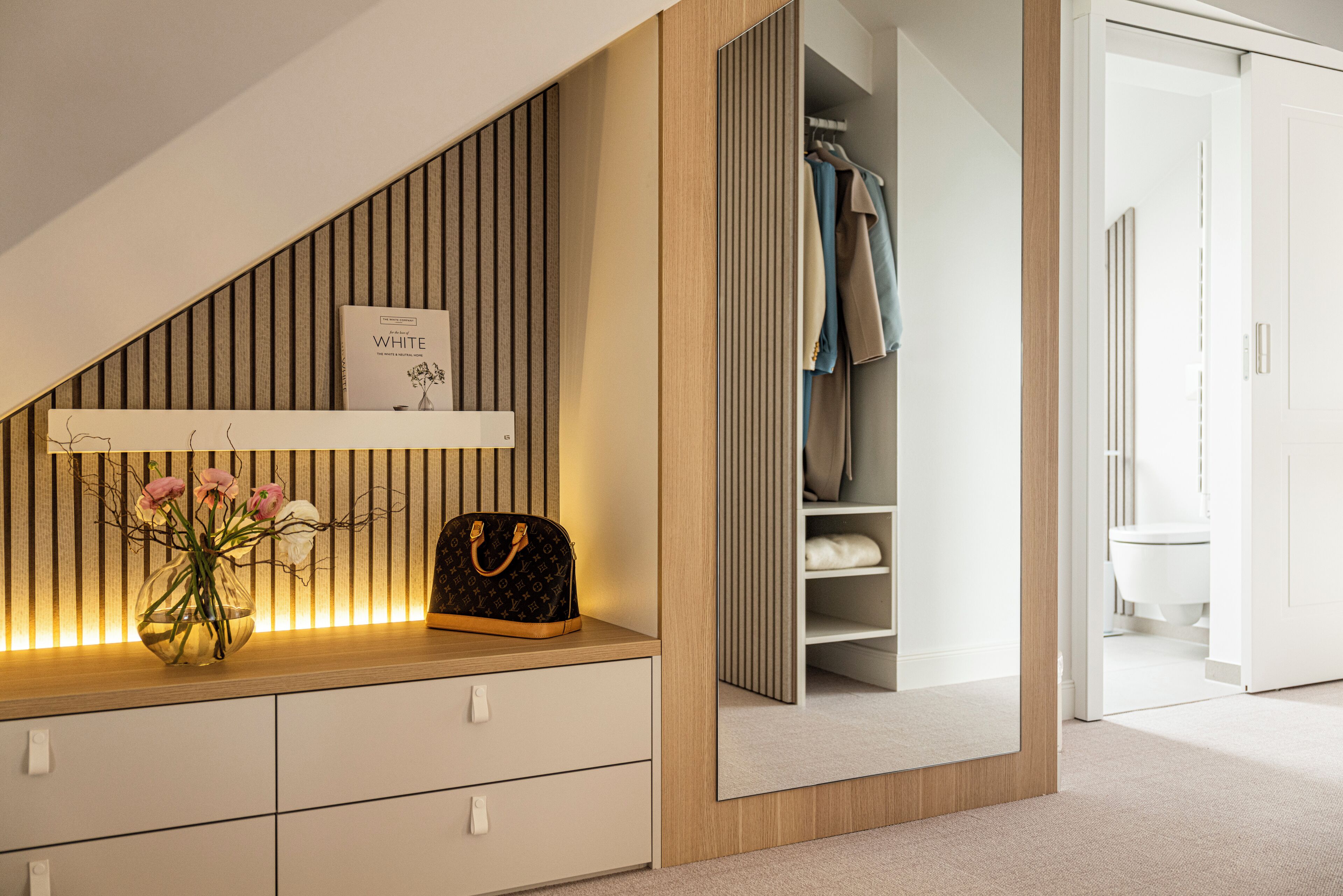 Ein modernes Schlafzimmer mit integriertem Kleiderschrank, einem Nachttisch mit Blumenvase und einer Pendelleuchte.
