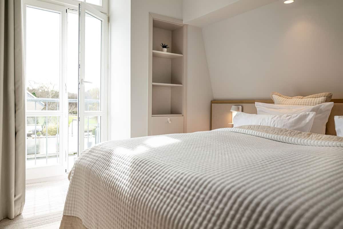 A bedroom with a large bed, a built-in shelf, and a view through an open door.