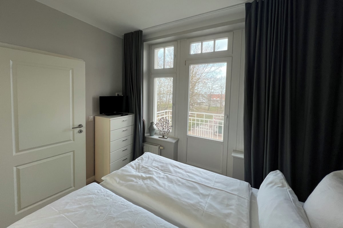 A hotel room with a bed, a dresser, a television on the dresser, a window with curtains, and a view of the outside.