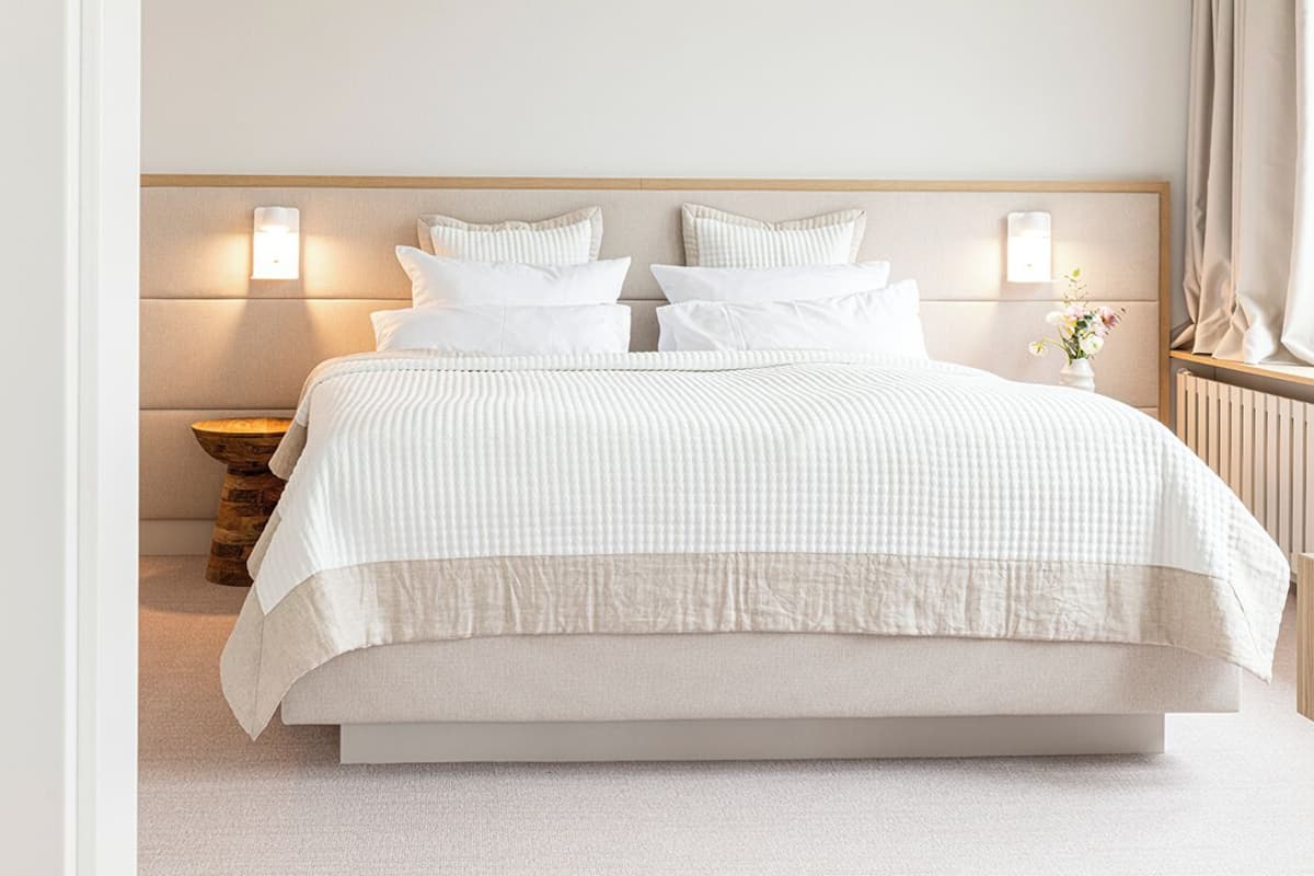 A neatly made double bed with a striped bedspread, two bedside tables with lamps, and a vase with flowers on the nightstand.