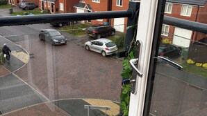 Blick aus einem Fenster auf einen Parkplatz mit Autos und einem Wohngebäude im Hintergrund.