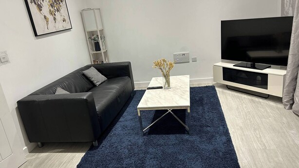 Ein modernes Wohnzimmer mit einem schwarzen Ledersofa, einem weißen Couchtisch, einem blauen Teppich, einer TV-Konsole und einer Weltkarte als Wandkunst.