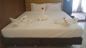 A hotel room with a large bed, a tufted headboard, white bedding, and decorative towels shaped like swans with red flowers. - Amman Cottage (Perundurai)