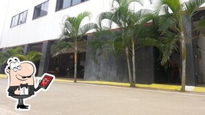A building with multiple windows and a covered entrance area with palm trees. - Amman Cottage (Perundurai)