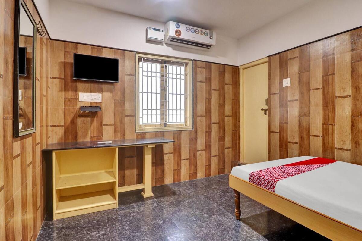 Un dormitorio con cama, escritorio, ventana y aire acondicionado.