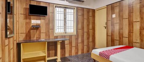 A bedroom with a bed, a desk, a window, and an air conditioning unit.