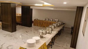 A buffet setup with multiple serving stations, a marble floor, and a yellow curtain backdrop. - Amman Cottage (Perundurai)