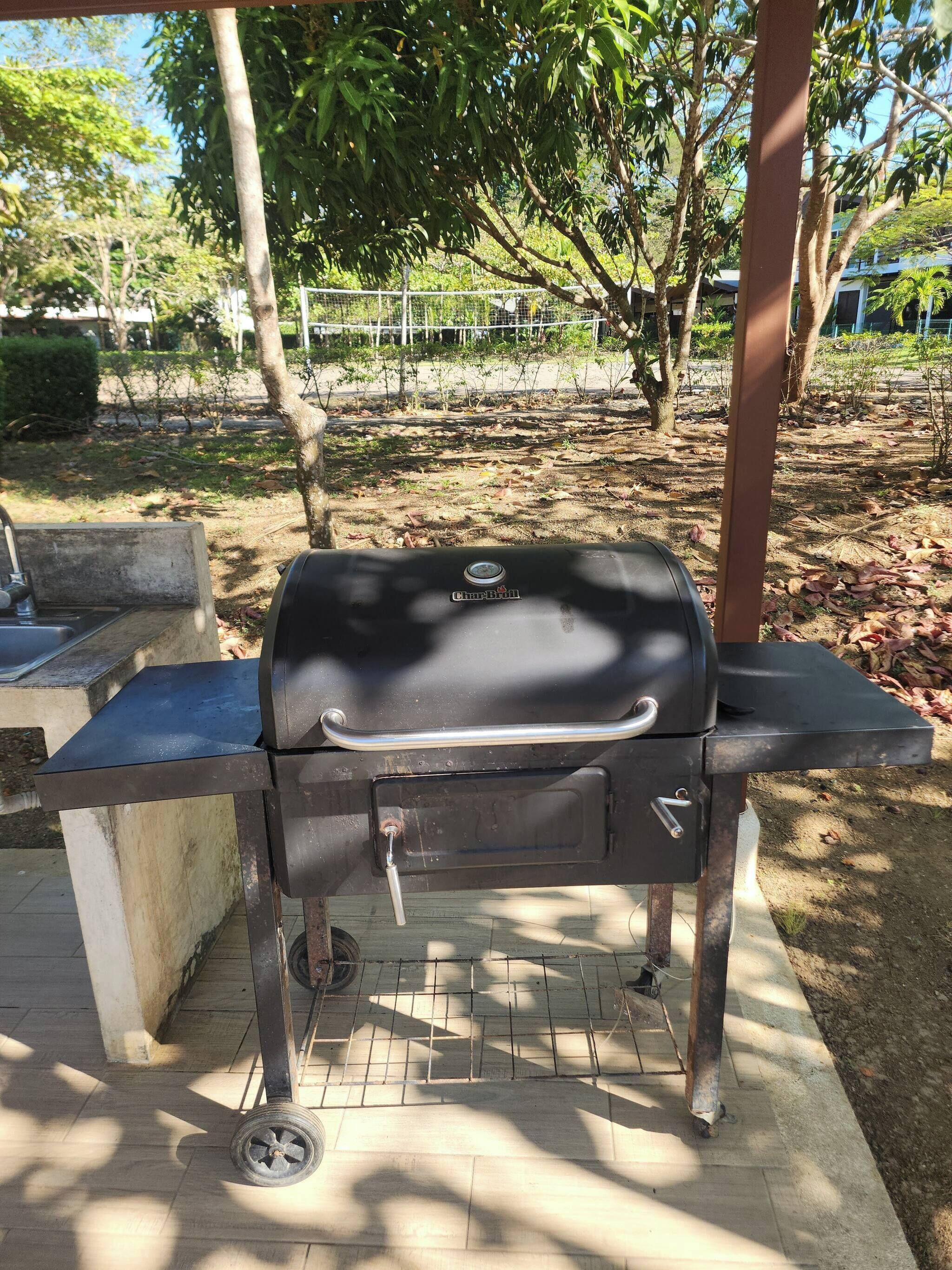 Una parrilla de carbón con asa y ruedas, sobre una superficie de hormigón con suelo de baldosas.