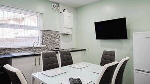 Eine moderne Küche mit Einbauherd, Spüle und einem Fenster mit Jalousien. An der Wand ist ein Flachbildfernseher befestigt und rechts daneben ein Kühlschrank.