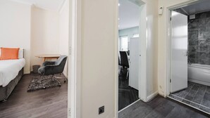 Ein Schlafzimmer mit Bett, Schreibtisch und Stuhl. Es gibt ein Badezimmer mit Badewanne und Dusche.