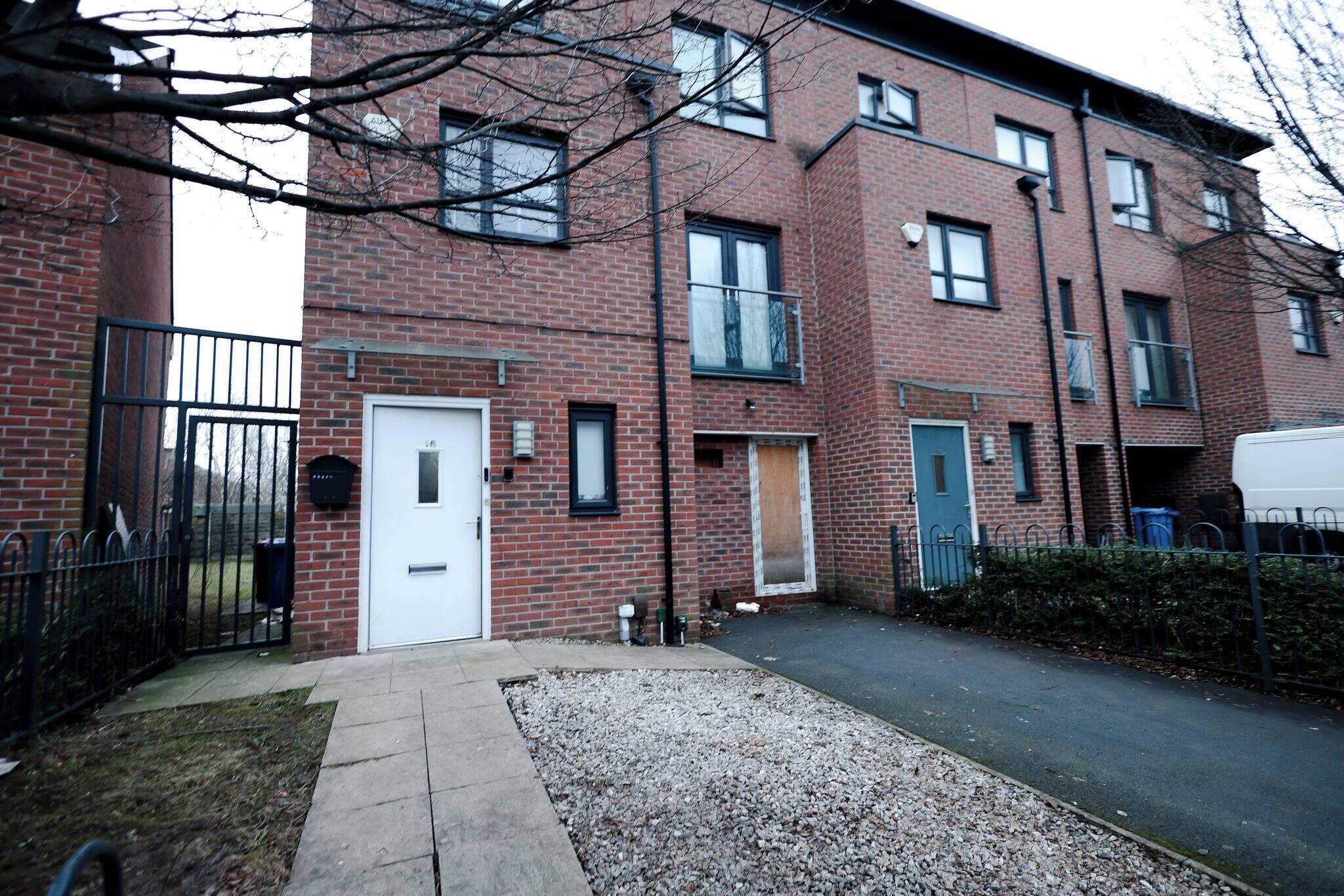 A multi-story brick building with a gated entrance, a white door, and a small garden area with gravel.