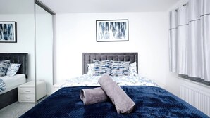 Une chambre à coucher avec un lit, une table de chevet, un miroir et une fenêtre avec des rideaux.
