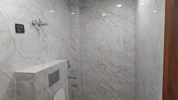 Un baño con paredes de mármol, inodoro y zona de ducha.
