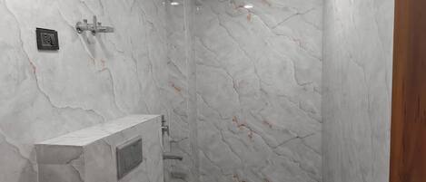 A bathroom with marble walls, a toilet, and a shower area.