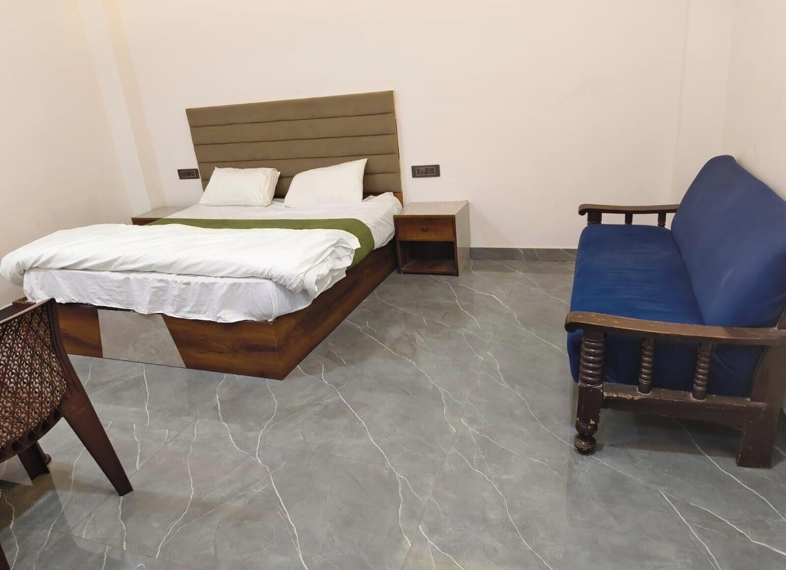 A bedroom with a bed, bedside table, chair, and a blue sofa.