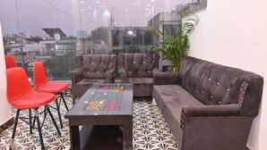 A modern lounge area with a glass partition, a brown sofa, red chairs, and a patterned table.