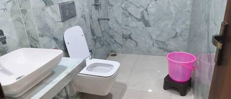 A bathroom with a marble wall, a toilet, a sink, and a pink trash bin.
