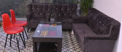 A living area with a dark brown sofa, two red chairs, and a glass coffee table with a geometric pattern.