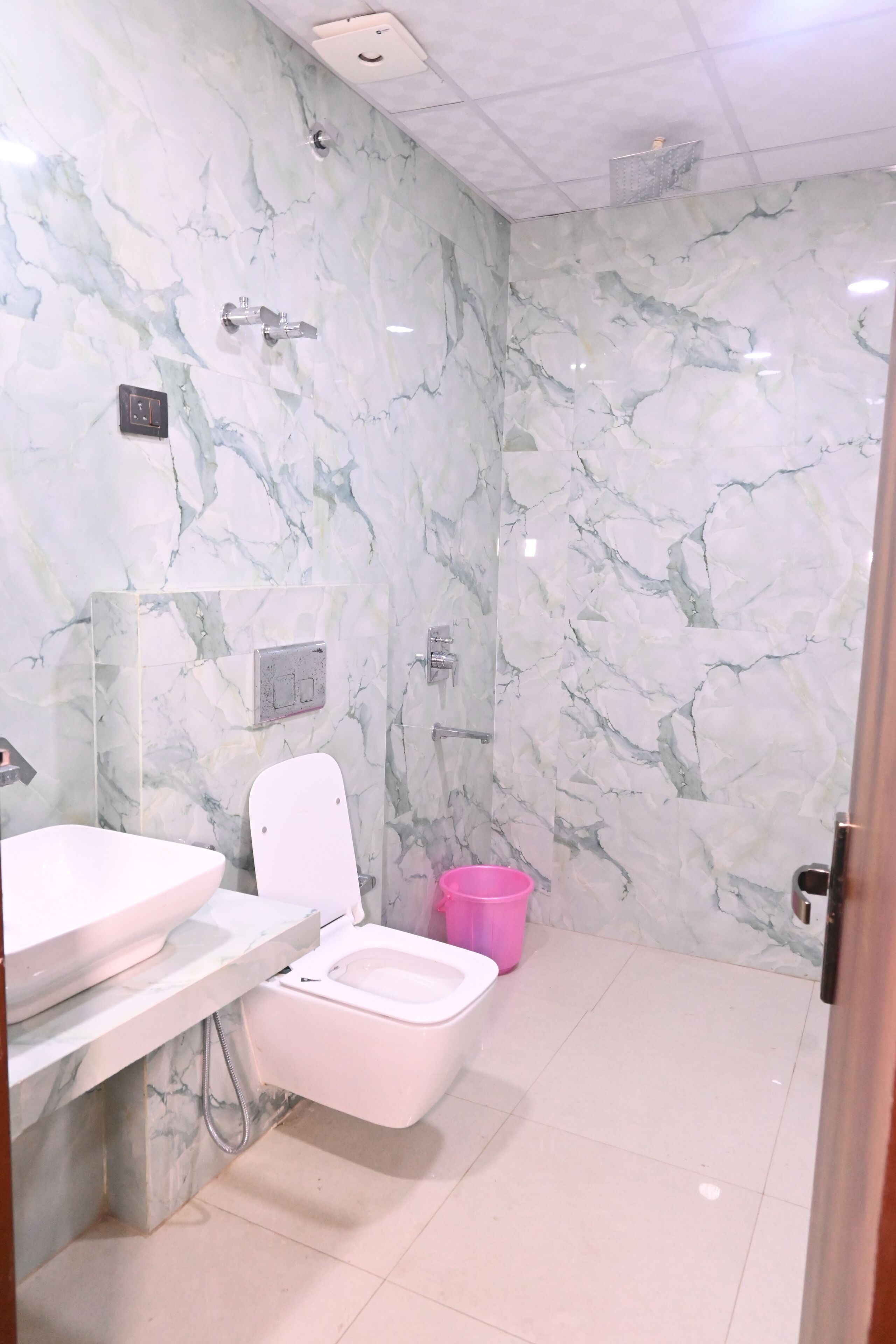 A bathroom with a marble wall, a sink, a toilet, and a shower.