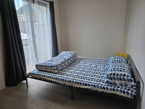 A small, single-bed room with a wooden floor, a window with sheer curtains, and a view of the outside. - Charming 3-Bedroom House in Bueng Kum, Thailand (Bueng Kum)