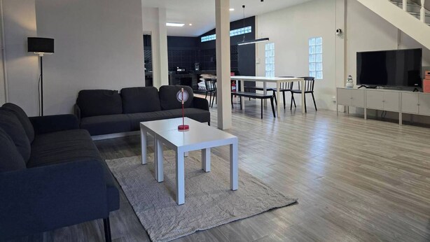 Ein modernes Wohnzimmer mit einer Couch, einem Couchtisch und einem Fernseher. Eine Treppe führt zu einer oberen Ebene.