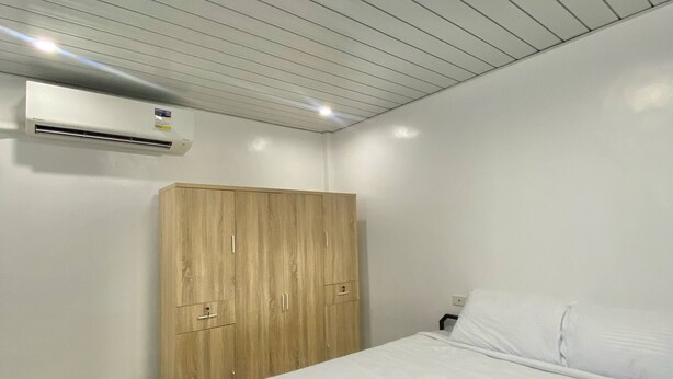 Una habitación de hotel con un armario de madera, una cama con ropa blanca y un equipo de aire acondicionado en la pared.