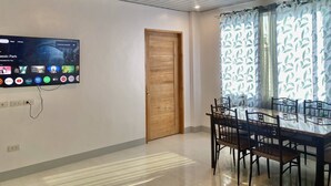 Uma sala de jantar moderna com porta de madeira, TV na parede exibindo aplicativos de streaming e mesa de jantar com cadeiras.