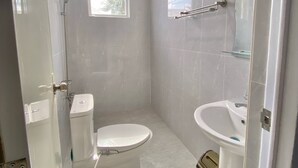 Uma casa de banho pequena e moderna, com sanita, lavatório e chuveiro.