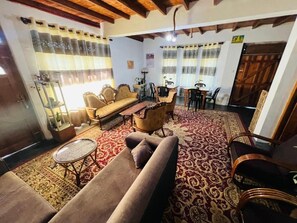A cozy living room with a sofa, armchairs, a coffee table, and a patterned rug. There is a dining area with a table and chairs. - Sasru Holiday Home (Nuwara Eliya)
