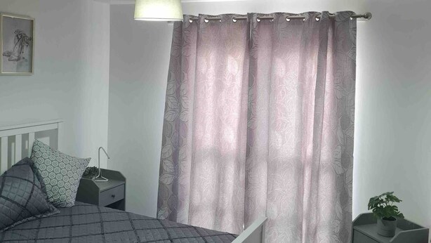 Ein Schlafzimmer mit einem Bett, Nachttischen, einer Lampe, einem Vorhang und einer kleinen Pflanze.