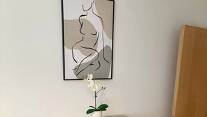 Ein Zimmer mit einer grauen Konsole, einem gerahmten abstrakten Kunstwerk und einer weißen Orchidee.