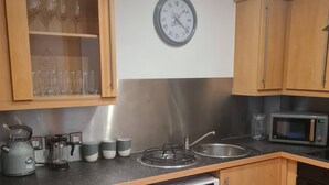 Eine kompakte Küche mit Holzausstattung, einer Waschmaschine, einer Mikrowelle und einer Wanduhr.