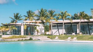 Un resort moderno con piscina, palmeras y un cielo azul despejado.