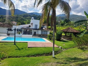 A house with a swimming pool, surrounded by lush greenery and mountains in the background.