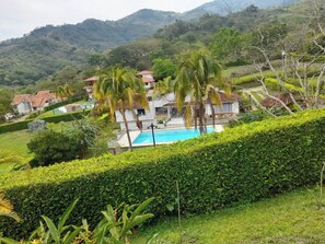 A hillside property with a swimming pool, lush greenery, and multiple houses with red-tiled roofs.