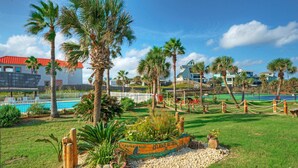 Een aangelegde tuin met palmbomen, een zwembad en een bootvormige plantenbak met de tekst 'Island Retreat'.