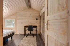 Ein Zimmer mit schrägem Dach, Holzwänden, einem Bett, einem Schreibtisch mit Stuhl und einem Fenster.