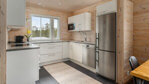 Une cuisine moderne avec des murs en bois, des armoires blanches, un réfrigérateur en acier inoxydable et une fenêtre donnant sur des arbres.