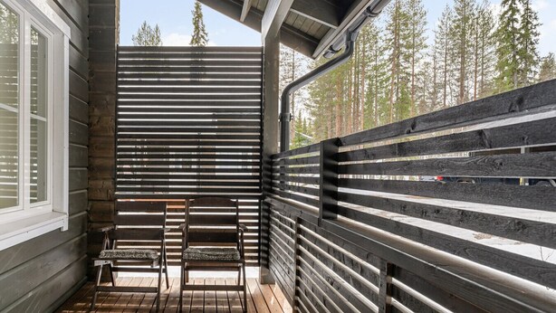 Une terrasse en bois avec deux chaises et une table, entourée d’une clôture métallique à lattes horizontales.